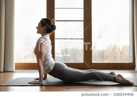 Side view smiling Indian woman doing upward facing dog exercise 108054406