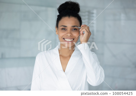 Smiling biracial woman pinch eyebrows with tweezers 108054425