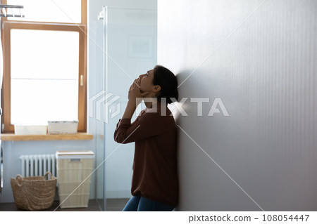 Frustrated depressed Indian woman crying, standing near wall at home 108054447