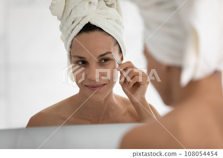Young woman look in mirror pinch eyebrows in bathroom Young woman look in mirror pinch eyebrows in bathroom 108054454