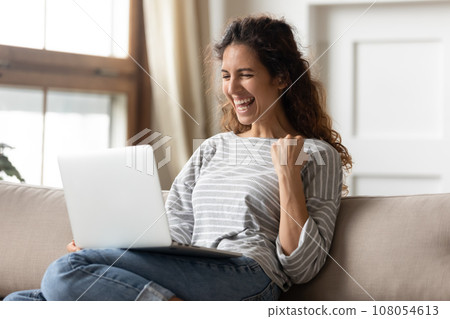 Excited millennial girl triumph win lottery on laptop Excited millennial girl triumph win lottery on laptop 108054613