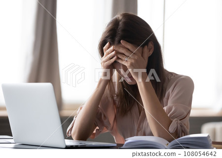 Woman sit at desk holding head with hands feels stressed Woman sit at desk holding head with hands feels stressed 108054642