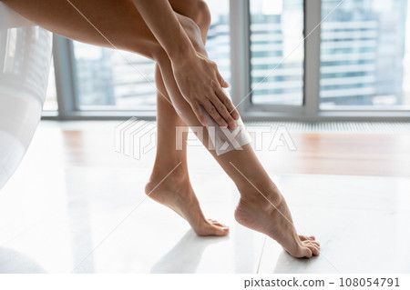 Close up of young woman use wax stripe on legs 108054791