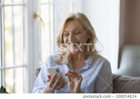 Cheerful senior blonde lady using online app on smartphone Cheerful senior blonde lady using online app on smartphone 108054814