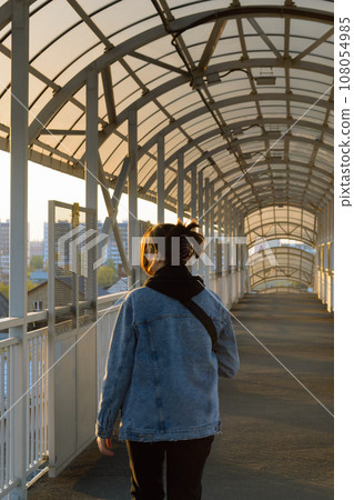 A photo of a girl from behind walking across a pedestrian bridge at sunset and looking to the left A photo of a girl from behind walking across a pedestrian bridge at sunset and looking to the left 108054985