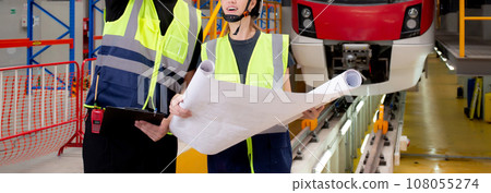 Young caucasian engineer man and woman or worker looking blueprint and checking electric train. 108055274