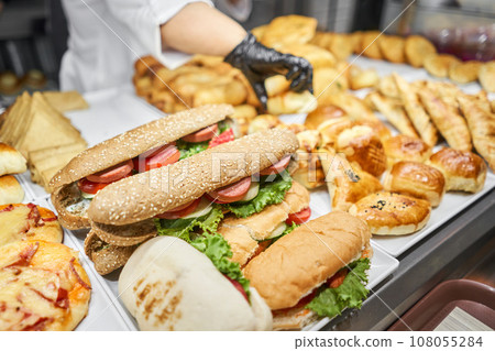Fresh sandwiches, pies and pizza to choose from in the window of a cafe, buffet or self-service cafe. Croissant with ham and cheese. Hot pastries lie on the shelf in the cafe. Buns in the store. Fresh sandwiches, pies and pizza to choose from in the window of a cafe, buffet or self-service cafe. Croissant with ham and cheese. Hot pastries lie on the shelf in the cafe. Buns in the store. 108055284