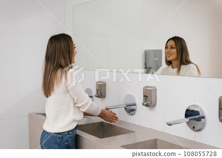 Women's hands under the water jet from the mixer. A middle-aged woman washes her hands in the bathroom 108055728