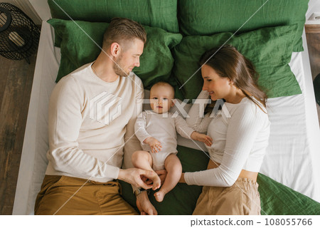 Young happy parents are lying on the bed with their baby son Young happy parents are lying on the bed with their baby son 108055766