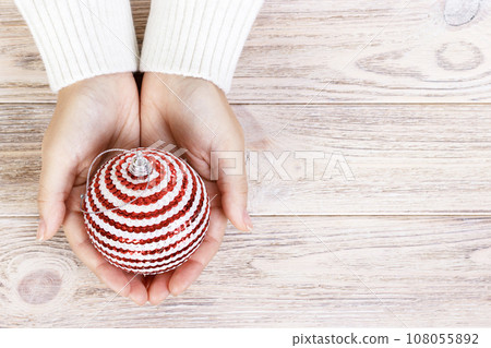 Christmas concept with hand and white ball - christmas tree toy. White round christmas ball in female hand. Wooden Background Christmas concept with hand and white ball - christmas tree toy. White round christmas ball in female hand. Wooden Background 108055892