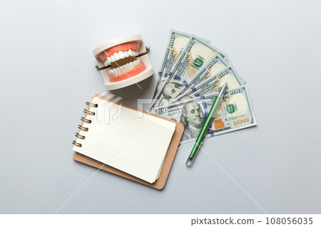 Flat lay composition with educational dental typodont model and money with notebook on colored table, top view. Expensive treatment Flat lay composition with educational dental typodont model and money with notebook on colored table, top view. Expensive treatment 108056035