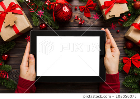 Christmas online shopping from home, female hands holding tablet pc with blank white display top view. woman hand holding tablet with blank screen, Christmas tree and gifts on background Christmas online shopping from home, female hands holding tablet pc with blank white display top view. woman hand holding tablet with blank screen, Christmas tree and gifts on background 108056075