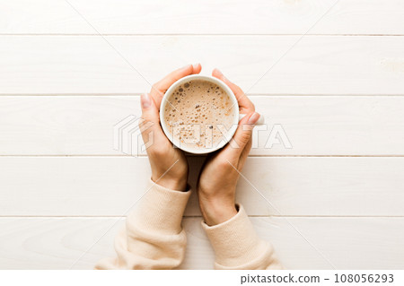 Minimalistic style woman hand holding a cup of coffee on Colored background. Flat lay, top view cappuccino cup. Empty place for text, copy space. Coffee addiction. Top view, flat lay Minimalistic style woman hand holding a cup of coffee on Colored background. Flat lay, top view cappuccino cup. Empty place for text, copy space. Coffee addiction. Top view, flat lay 108056293