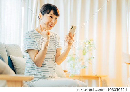 一名中年婦女在客廳裡看著智能手機 一名中年婦女在客廳裡看著智能手機 108056724