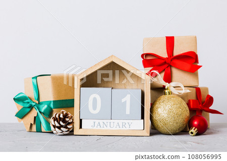 1 january. Christmas composition on colored background with a wooden calendar, with a gift box, toys, bauble copy space 1 january. Christmas composition on colored background with a wooden calendar, with a gift box, toys, bauble copy space 108056995