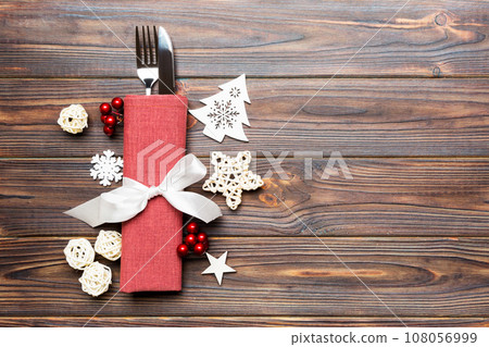 Top view of fork and knife on napkin on wooden background. Different christmas decorations and toys. New Year dinner concept with empty space for your design 108056999