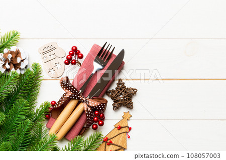 Top view of fork and knife on napkin with christmas decorations and new year tree on wooden background. Holiday and festive concept with copy space Top view of fork and knife on napkin with christmas decorations and new year tree on wooden background. Holiday and festive concept with copy space 108057003