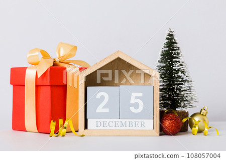 25 december. Christmas composition on colored background with a wooden calendar, with a gift box, toys, bauble copy space 108057004