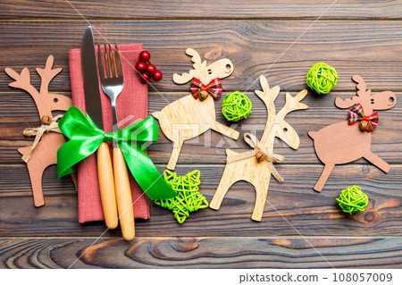 Top view of new year utensils on napkin with holiday decorations and reindeer on wooden background. Close up of christmas dinner concept 108057009