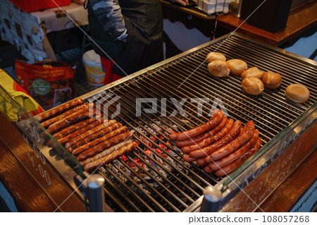 Dusselldorf, Germany - December 13, 2022: different types of christmas goodies xmas market. Grilling sausages on barbecue grill at food stall of Christmas market winter wonderland 108057268