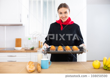 Happy female chef in black uniform offering freshly baked muffins Happy female chef in black uniform offering freshly baked muffins 108058500