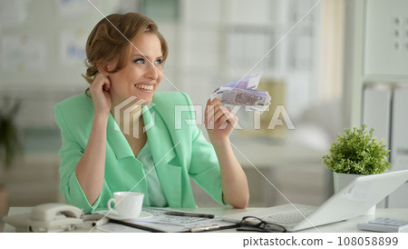 Smiling young businesswoman holding banknotes Smiling young businesswoman holding banknotes 108058899