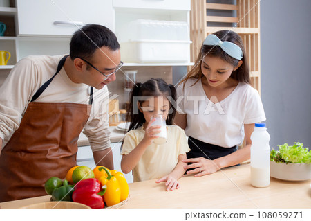 Happy family with father, mother and daughter in kitchen drinking milk in glass for healthy together 108059271