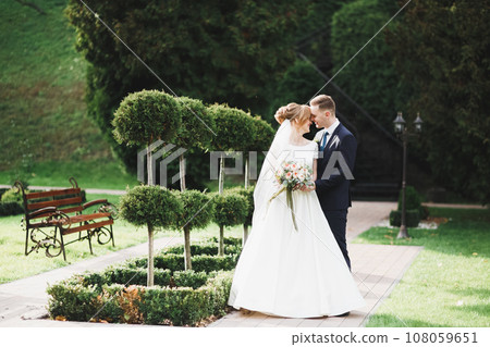 Stylish couple of happy newlyweds walking in the park on their wedding day with bouquet Stylish couple of happy newlyweds walking in the park on their wedding day with bouquet 108059651