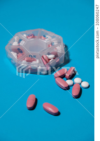 Organizer weekly shots on blue background with Copy space for your text. Closeup of medical pill box with doses of tablets for daily take medicine with white pink drugs and capsules. Daily vitamins at 108060247