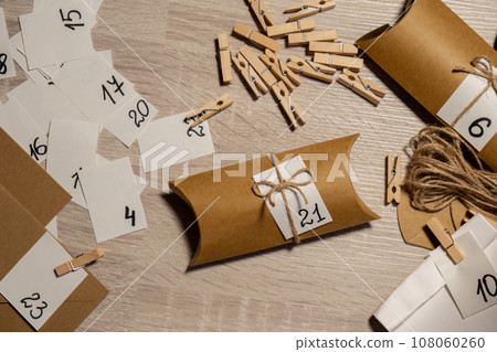 Unrecognizable young woman sticks number on craft bag, fastens with clothespin. Female making kraft paper for homemade advent calendar Made with your own hands step by step DIY crafts do it yourself 108060260