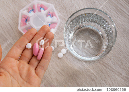 Woman sorting pills Organizer weekly shots Closeup of medical pill box with doses of tablets for daily take medicine with white pink drugs and capsules. Young woman getting her daily vitamins at home 108060266