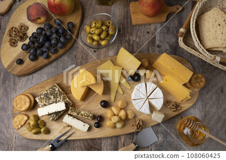 Cheese assorted on a wooden board, rustic style. Several sliced cheeses with pears, peaches, grapes, olives, honey, bread, crackers and walnuts. Selective focus, close-up. Cheese assorted on a wooden board, rustic style. Several sliced cheeses with pears, peaches, grapes, olives, honey, bread, crackers and walnuts. Selective focus, close-up. 108060425