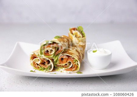 Pancakes with salmon (trout), sour cream and greenstuff. Thin, not sweet blinchiki stuffed with red fish. Traditional Russian and Ukrainian dish. Feast of Maslenitsa. Selective focus, close-up. Pancakes with salmon (trout), sour cream and greenstuff. Thin, not sweet blinchiki stuffed with red fish. Traditional Russian and Ukrainian dish. Feast of Maslenitsa. Selective focus, close-up. 108060426