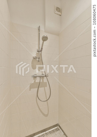 a shower stall in a tiled bathroom with white tiles on the walls, and a chrome hand rail attached to the wall 108060475