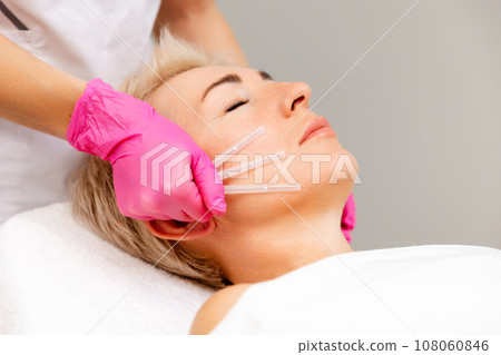 Thread lifting. Professional beautician in medical gloves holding needles. Close up face of adult pretty woman 108060846