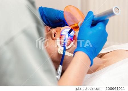 Close-up view of young Caucasian woman lying at reception in dental office. Dentist puts seal on client's sick tooth. Concept of dentistry and orthodontics 108061011