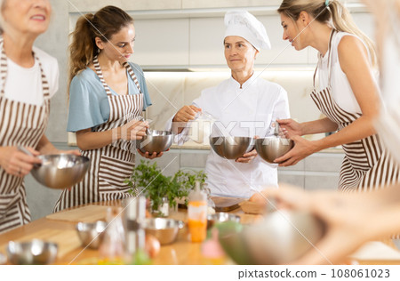 Elderly woman chef with bowl in hands tells women at culinary courses about traditions of cuisine Elderly woman chef with bowl in hands tells women at culinary courses about traditions of cuisine 108061023