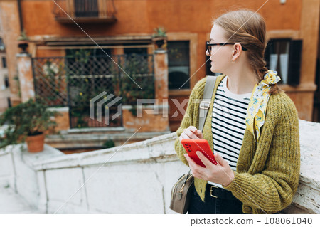 A portrait of a smiling beautiful woman walking with phone on urban background. Happy women in dress is using a smartphone outdoors. Urban lifestyle concept A portrait of a smiling beautiful woman walking with phone on urban background. Happy women in dress is using a smartphone outdoors. Urban lifestyle concept 108061040