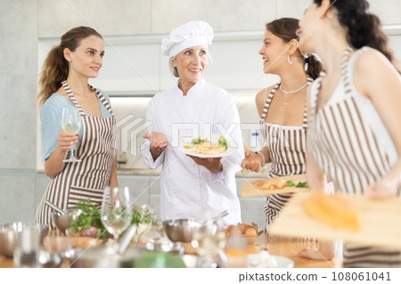 Mature female cook holding plate with cooked chicken Mature female cook holding plate with cooked chicken 108061041
