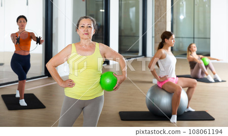 Mature female performing set of exercises with pilates ball 108061194