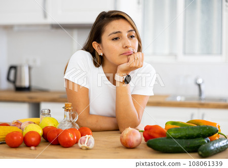 Sad woman looking at vegetable at kitchen, dieting problems 108061339