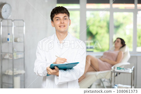 Young man doctor posing in doctor's cabinet with document in hands 108061373