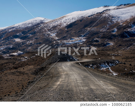 Mountain track off-road to a high-mountain village. Snow-covered narrow mountain road on the slope of snow mountains. Dangerous off-road driving along the mountains to the edge and steep cliffs. 108062185