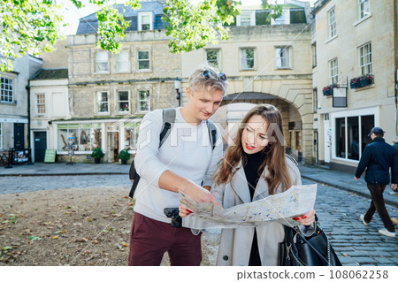 Fun, friends, travel and tourism concept. Young couple looking for direction during travel walk in old European city. Tourists consulting with a city guide map . Explore a new city together. 108062258