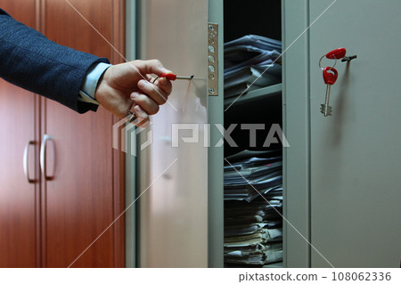 Documents are in the closet. Secret documentation. Document storage. Man opens a metal cabinet with documents. A hand with a key. Documents are in the closet. Secret documentation. Document storage. Man opens a metal cabinet with documents. A hand with a key. 108062336