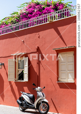 black and white scooter is parking in front of red house on the street in Chania, Crete 108062367