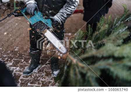 Man cuts a part of the trunk from a Christmas tree with a chainsaw 108063740
