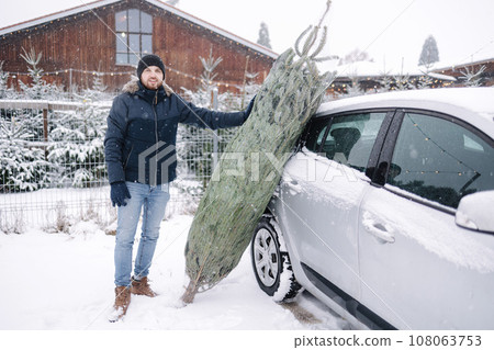Handsome bearded man stand by the car and think how to put a Christmas tree into car 108063753