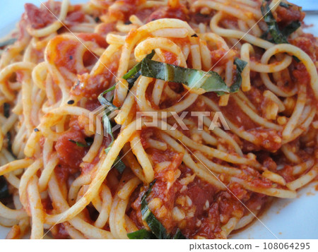 spaghetti with tomato sauce close-up bits of greens 108064295