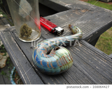 Jar of Medical Marijuana, Pipe and lighter sitting on a well used unpainted wood rai 108064427
